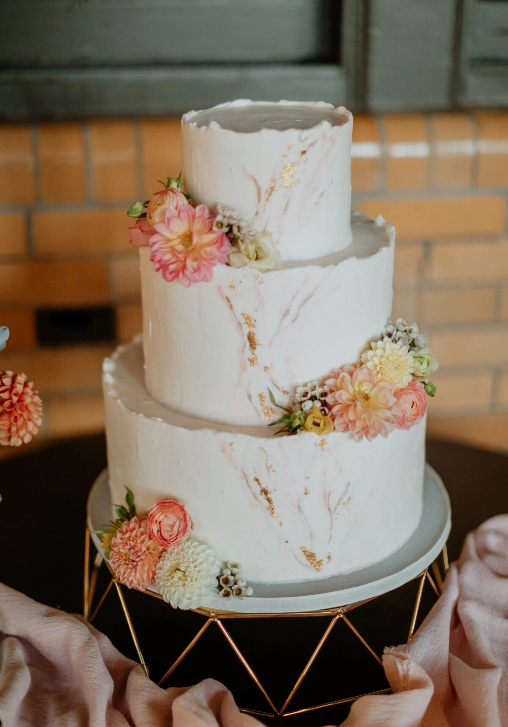 One of our beautiful modern wedding cakes designed with gold and floral accents on modern cake stand